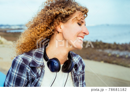 Close up smiling curly hair caucasian woman with large headphones walking outdoor. Enjoy the moment and music. Freedom and happiness, simple pleasures concept. Close up smiling curly hair caucasian woman with large headphones walking outdoor. Enjoy the moment and music. Freedom and happiness, simple pleasures concept. 78681182