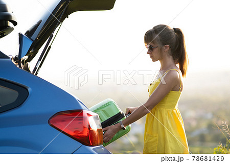 A woman in yellow dress taking green suitcase from car trunk. Travel and vacations concept. A woman in yellow dress taking green suitcase from car trunk. Travel and vacations concept. 78681429