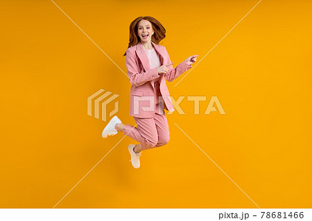 Successful business woman in suit jumping pinting index finger at side, isolated on yellow background 78681466