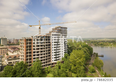 Apartment or office tall building unfinished under construction among green tree tops. Tower cranes on bright blue sky copy space background. 78682035