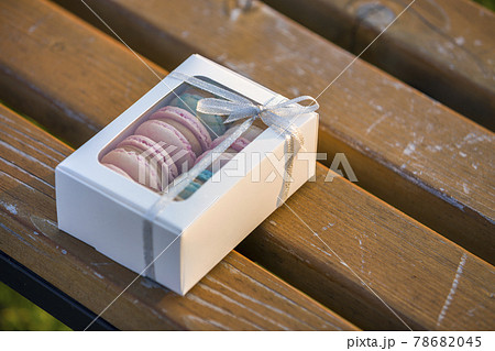 Cardboard white gift box with colorful handmade macaron cookies on wooden bench outdoors. Cardboard white gift box with colorful handmade macaron cookies on wooden bench outdoors. 78682045