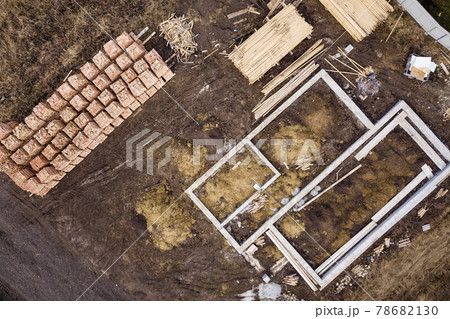 Concrete foundation for basement of future house, stacks of bricks and building timber logs for construction on sunny summer day, aerial view. Concrete foundation for basement of future house, stacks of bricks and building timber logs for construction on sunny summer day, aerial view. 78682130