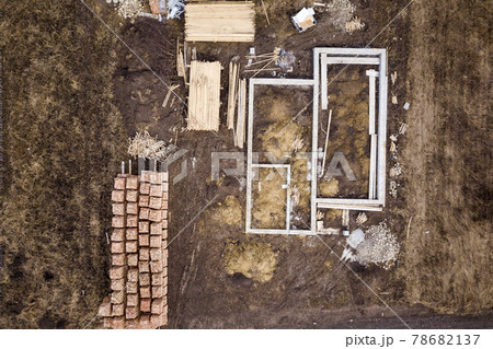 Concrete foundation for basement of future house, stacks of bricks and building timber logs for construction on sunny summer day, aerial view. Concrete foundation for basement of future house, stacks of bricks and building timber logs for construction on sunny summer day, aerial view. 78682137