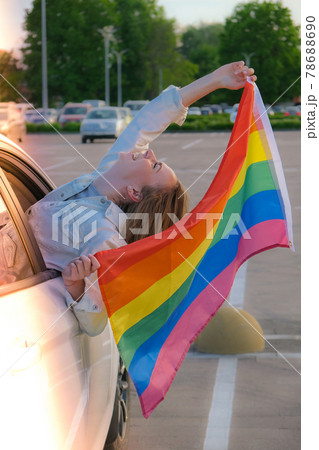 Young blonde millennial woman with LGBTQ flag looking from car window. Rainbow LGBT flag. Peace and freedom the symbol of LGBT, spending and sharing loving time. Support LGBTQ community 78688690