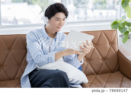 自宅でヘッドフォンをしてタブレットを見る若い男性 78689147