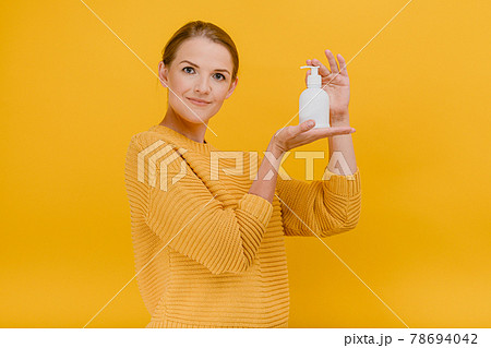Beautiful pretty woman casually dressed uses an antiseptic sanitizer or liquid soap, calmly looks at the camera, Hygiene, cleaning concept standing isolated against a yellow background 78694042