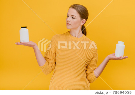 Beautiful pretty woman choosing bottle of medical pills or vitamins casually dressed , having doubtful expression      treatment and prevention of diseases medical pills vitamins concept standing 78694059