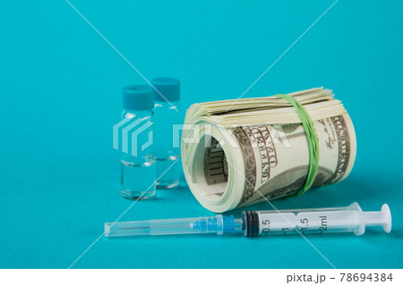 a roll of dollars lies on a turquoise background, a vaccine and a syringe are nearby, the concept of financing universal vaccination 78694384