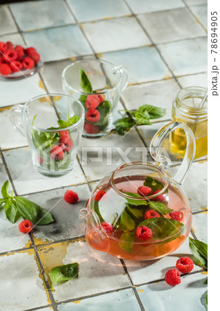 Hot raspberry tea in transparent teapot on a stone table. Fresh berries, mint, glass cup Hot raspberry tea in transparent teapot on a stone table. Fresh berries, mint, glass cup 78694905