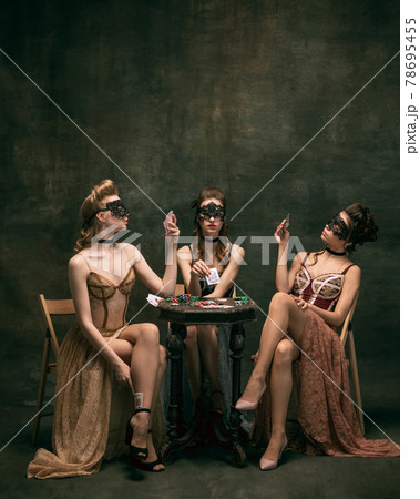 Pretty women in vintage 20s dresses. Young girls in art action sitting together and posing on wall background. 78695455