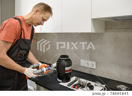 The worker is installing a household waste shredder for the kitchen sink. 78695845