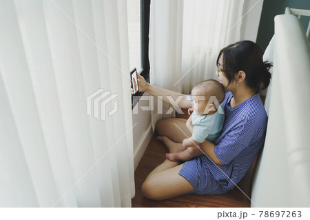 Asian mother and newborn baby boy doing online video call with family on smartphone  78697263
