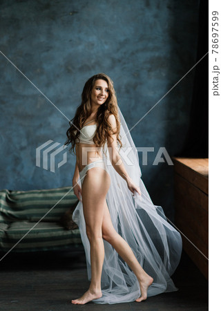 Beautiful woman in lingerie showing long legs sexy pose standing at bed over her bedroom near big window. Bride boudoir. Wedding morning. 78697599