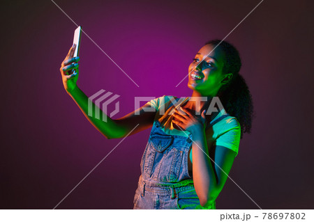 Latino young woman with phone isolated on studio background in neon. Concept of human emotions, facial expression. 78697802