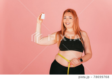 Cheerful plus size woman wearing sporty outfit measuring her waist Cheerful plus size woman wearing sporty outfit measuring her waist 78699768