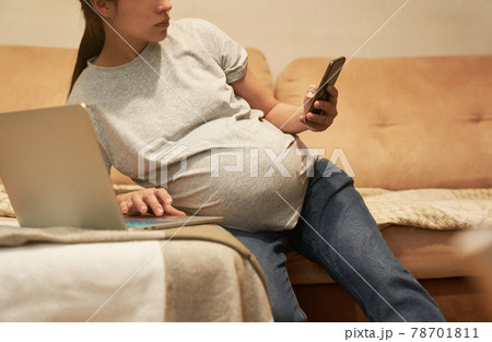 Pregnant woman at home with phone is sitting with computer, online shopping 78701811
