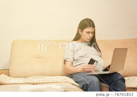 Pregnant woman at home with phone is sitting with computer, online shopping 78701852