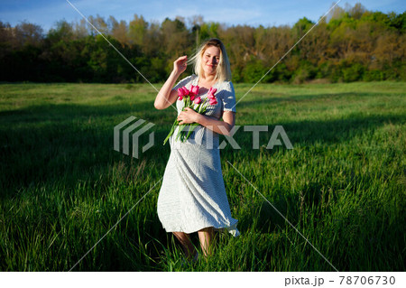 pregnant woman on a green meadow walking with a bouquet of flowers 78706730