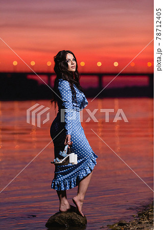 Beautiful young girl with long dark wavy hair standing at the bank of the river Beautiful young girl with long dark wavy hair standing at the bank of the river 78712405