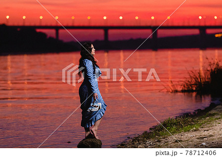 Beautiful young girl with long dark wavy hair standing at the bank of the river Beautiful young girl with long dark wavy hair standing at the bank of the river 78712406