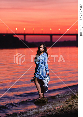 Beautiful young girl with long dark wavy hair standing at the bank of the river Beautiful young girl with long dark wavy hair standing at the bank of the river 78712407