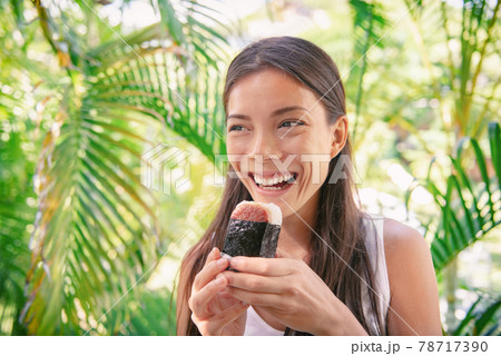 Spam musubi rice ball sandwich Asian woman tourist eating japanese snack food typical of hawaiian market in Hawaii. 78717390