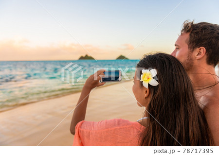 Hawaii vacation tourists taking photo with phone on romantic walk at sunset on Lanikai beach, Oahu, Hawaii honeymoon getaway. Couple holiday lifestyle. Hawaii vacation tourists taking photo with phone on romantic walk at sunset on Lanikai beach, Oahu, Hawaii honeymoon getaway. Couple holiday lifestyle. 78717395