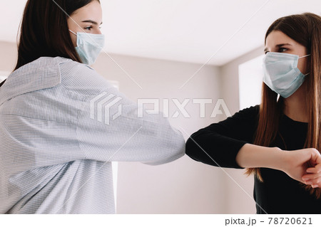 Two smiling girls in protective face mask say hello with elbow Two smiling girls in protective face mask say hello with elbow 78720621