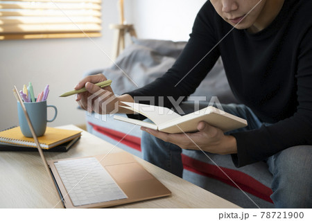 Young man using laptop and reading information on notebook while siting on sofa. 78721900