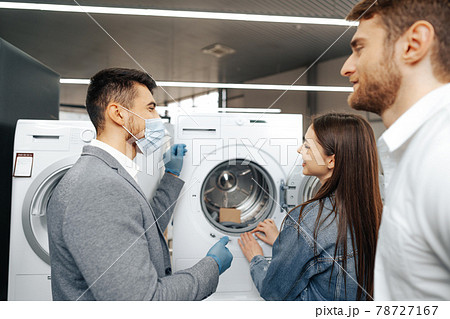 Salesman in hypermarket wearing medical mask demonstrates his clients a new washing machine 78727167