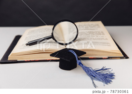 Magnifier on open book and graduation cap on white table. Education concept Magnifier on open book and graduation cap on white table. Education concept 78730361