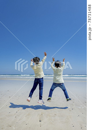 海辺でジャンプする姉と弟の後ろ姿の写真素材