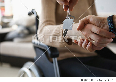 Disabled woman in wheelchair shaking hands with man with keys to new apartment closeup 78737917
