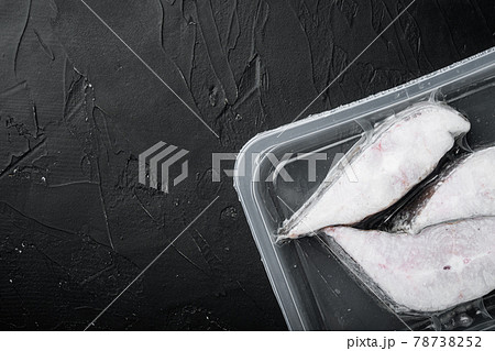 Frozen Greenland halibut steaks vacuum pack, on black dark stone table background, top view flat lay, with copy space for text 78738252