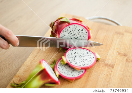 Female hands is cutting a dragon fruit or pitaya with pink skin and white pulp with black seeds on wooden cut board on the table. Exotic fruits, healthy eating concept 78746954