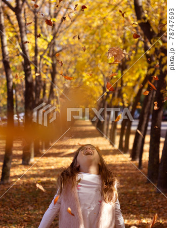 Beautiful little girl throwing fallen leaves, playing in the park; autumn/nature background 78747693