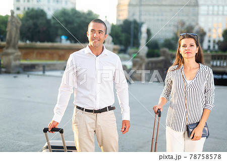 Traveling spouses strolling with luggage along city street 78758578