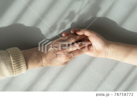 カーテン越しの光の下で愛しい孫の手をつかむ祖母の手 78758772