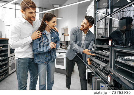 Male shop assistant helps young couple to choose new home appliance 78762950