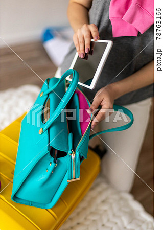 Woman hands ready travel journey putting tablet pc into handbag packing baggage at bedroom Woman hands ready travel journey putting tablet pc into handbag packing baggage at bedroom 78763166