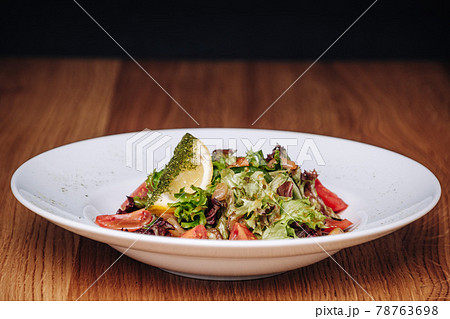 White Plate with Salad Stands on a Wooden Table in a Restaurant 78763698