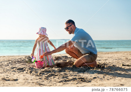 father and daughter playing with toys on beach 78766075