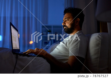 indian man with laptop in bed at home at night 78767527