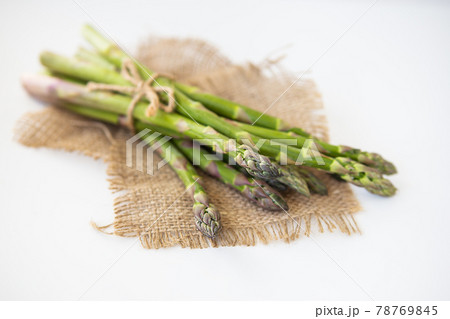 Fresh green asparagus tied with thread and lying on sacking. Healthy and wholesome food concept. Fresh green asparagus tied with thread and lying on sacking. Healthy and wholesome food concept. 78769845