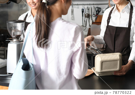 飲食店で働くエプロン姿の女性とお客のテイクアウトイメージ 78770322