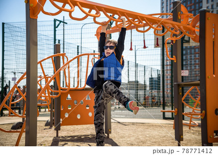 Cute boy is climbing on the playground in the schoolyard. He has a very happy face and enjoy this adventure sports alone outdoor. Warm sunny day 78771412
