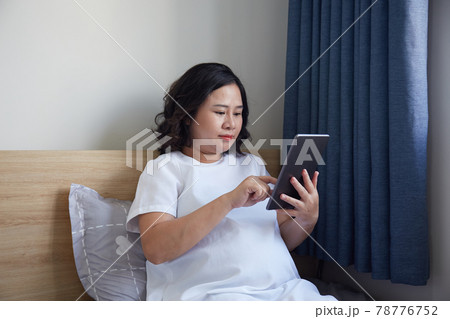 Young Asian Pregnant Woman using digital pen for drawing and taking note on her digital tablet at home near the window	 78776752