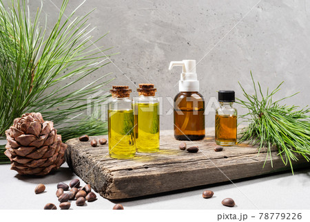 Composition of set of small glass bottles of essential cedar oil on old wooden board with cedar branches, cone and nuts on grey. Herbal medicine, spa coniferous concept. Copy space. Horizontal photo. 78779226