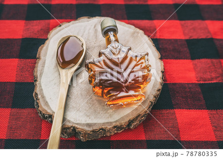 Maple syrup bottle Quebec cultural food traditional harvest top view on buffalo dining tablecloth background. Canada grade A amber sweet liquid in wooden spoon from sugar shack cabane a sucre farm 78780335