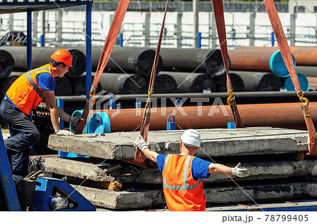 Two slingers unload concrete slabs on the street on a summer day. Workers in construction helmets 78799405
